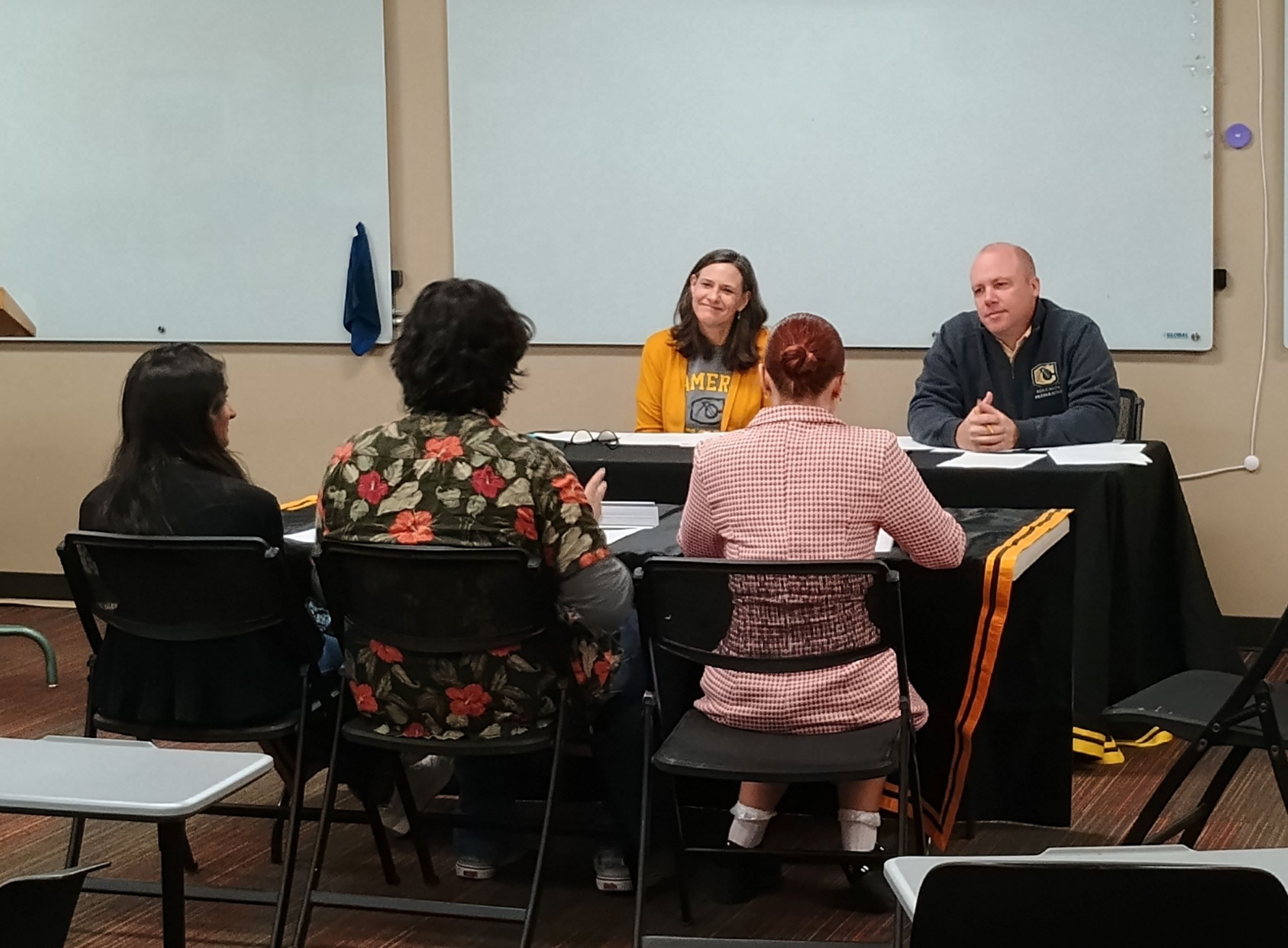 Three high school students sit across Professor Sarah Janda and Instructor Travis Childs to defend their prepared thesis.